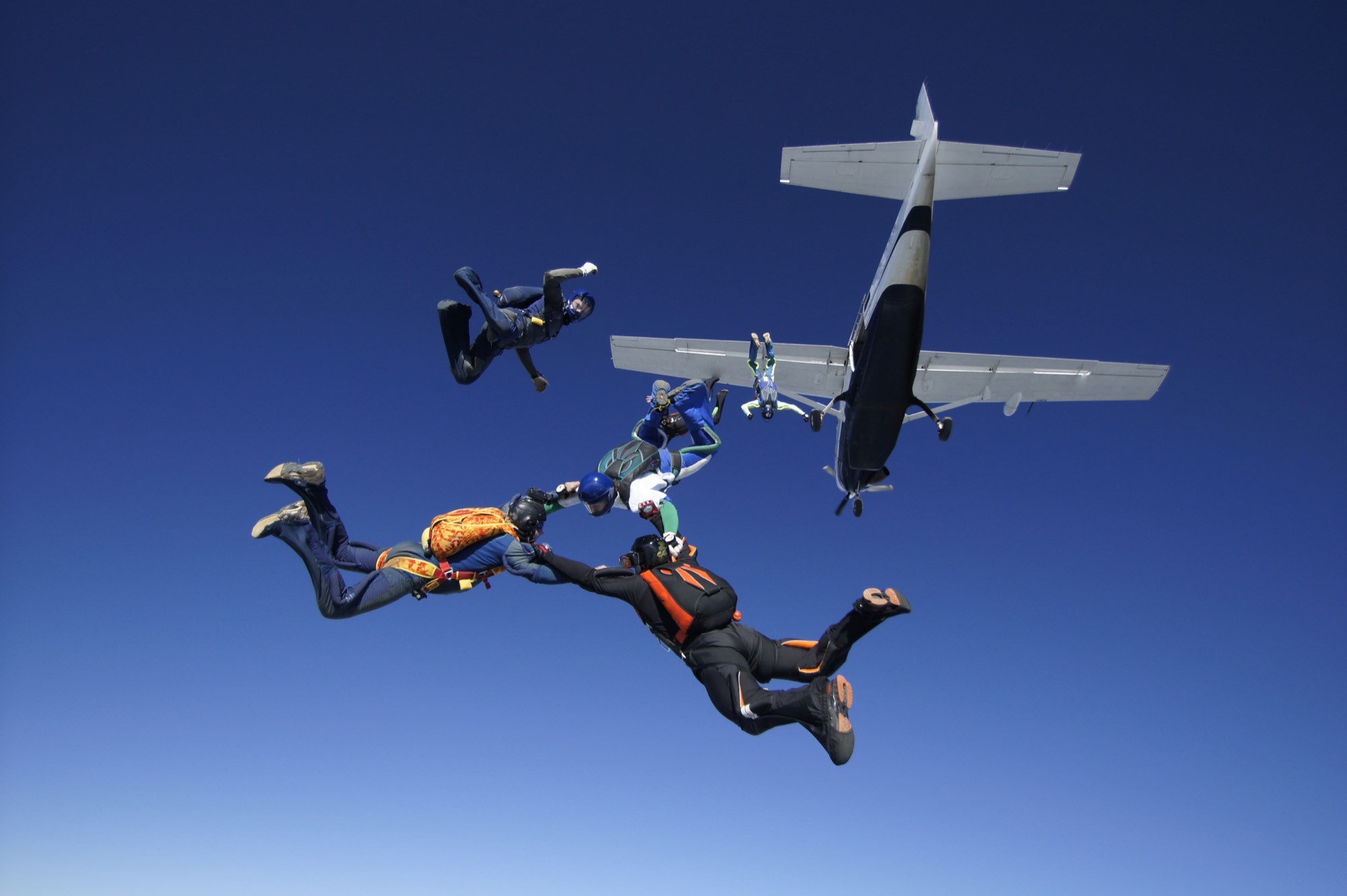 A team of skydivers in free fall, holding on to one another in formation, with the aircraft they jumped from above them